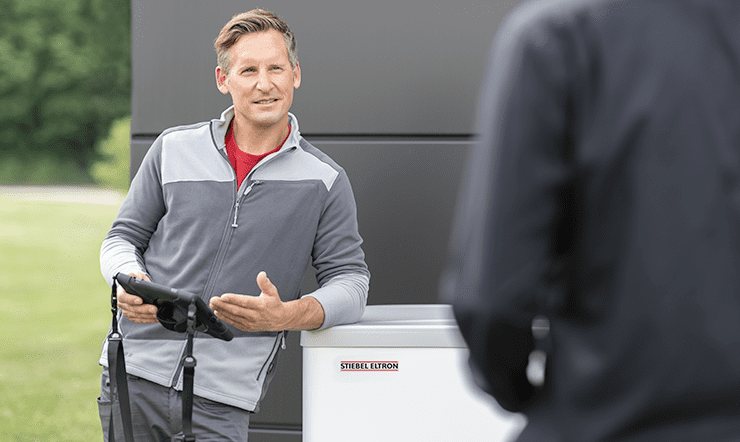 A mid-age white man leans on a Stiebel Eltron heat pump, holding an electronic tablet