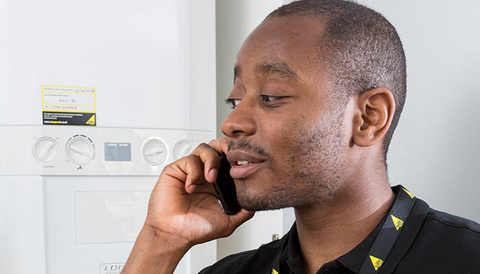 A gas engineer on the phone, standing in front of a boiler