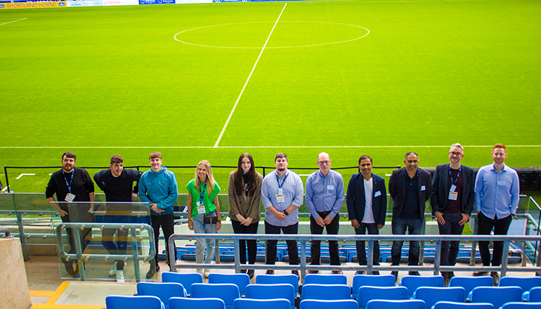 Baxi's first cohort of apprentice graduates standing in front of the pitch at the Coventry Building Society Arena